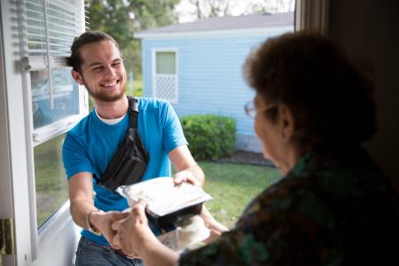 A smiling volunteer hands a client their meal