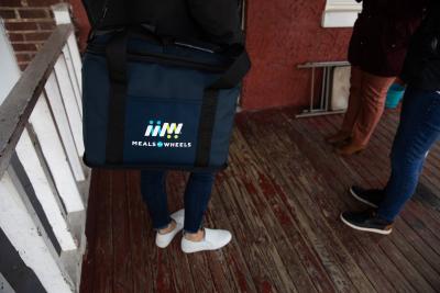 The feet of three volunteers are visible, with the low slung bag of Meals on Wheels Meals