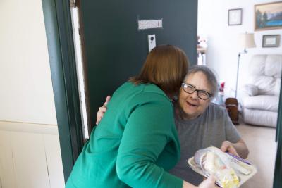 A volunteer hugs a client who is holding a meal